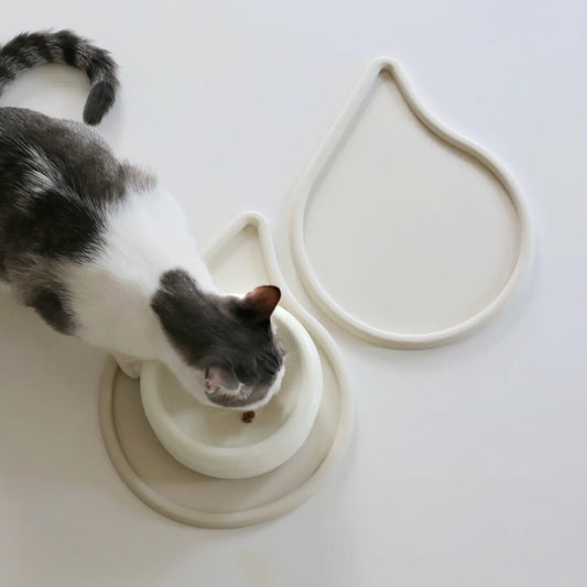 Gråvit katt vid två sandfärgade matskålsunderlägg som har lagts ihop så de blir en enhetlig matplats