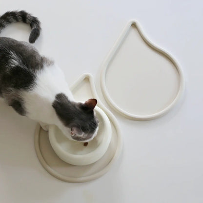 Gråvit katt vid två sandfärgade matskålsunderlägg som har lagts ihop så de blir en enhetlig matplats 