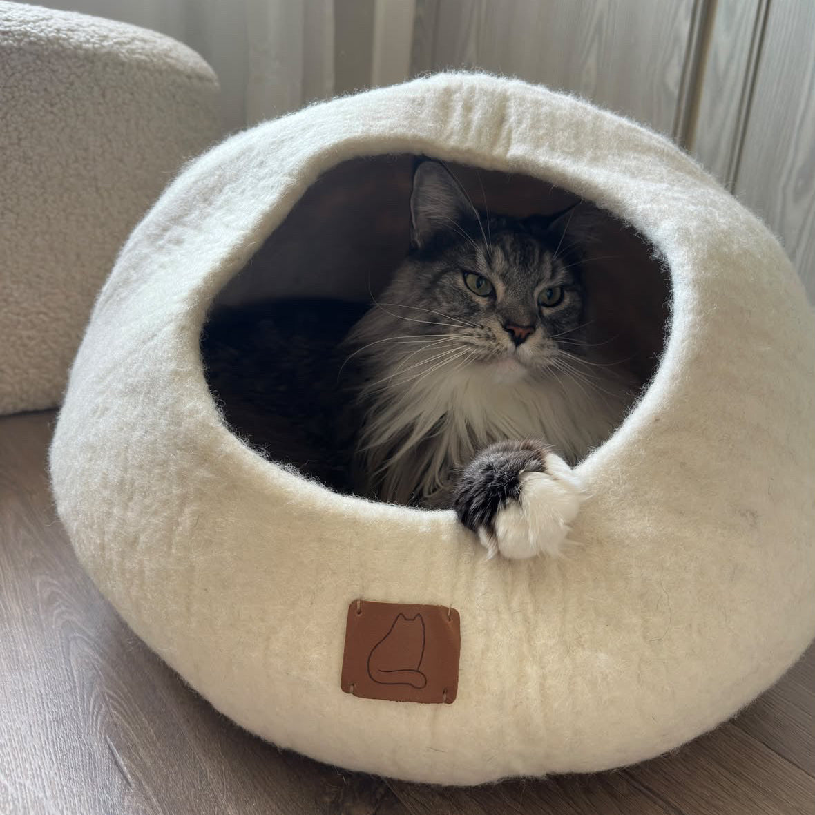 En stor, fluffig långhårig katt som ligger bekvämt inuti en extra stor snövit kattgrotta i ekologisk ull